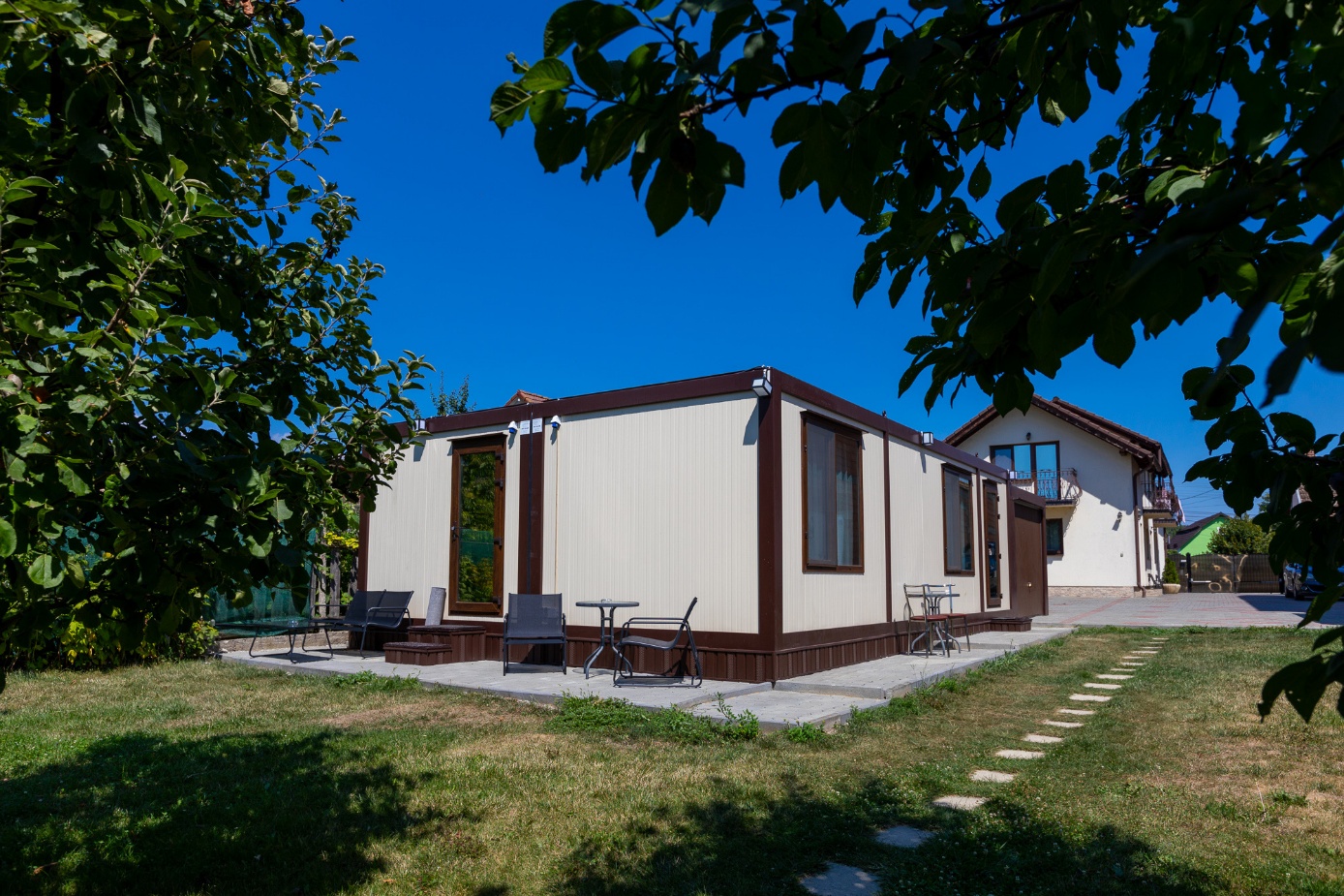 Casă din containere amplasată în curte, cu terasă exterioară, ferestre mari și spațiu verde amenajat pentru locuire modernă.