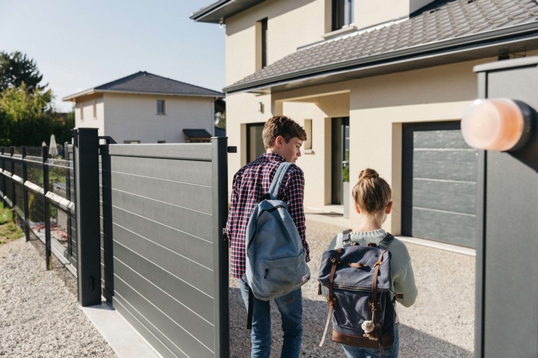 Familie intrând într-o casă modernă cu poartă automatizată și sistem smart home Somfy integrat discret în design.