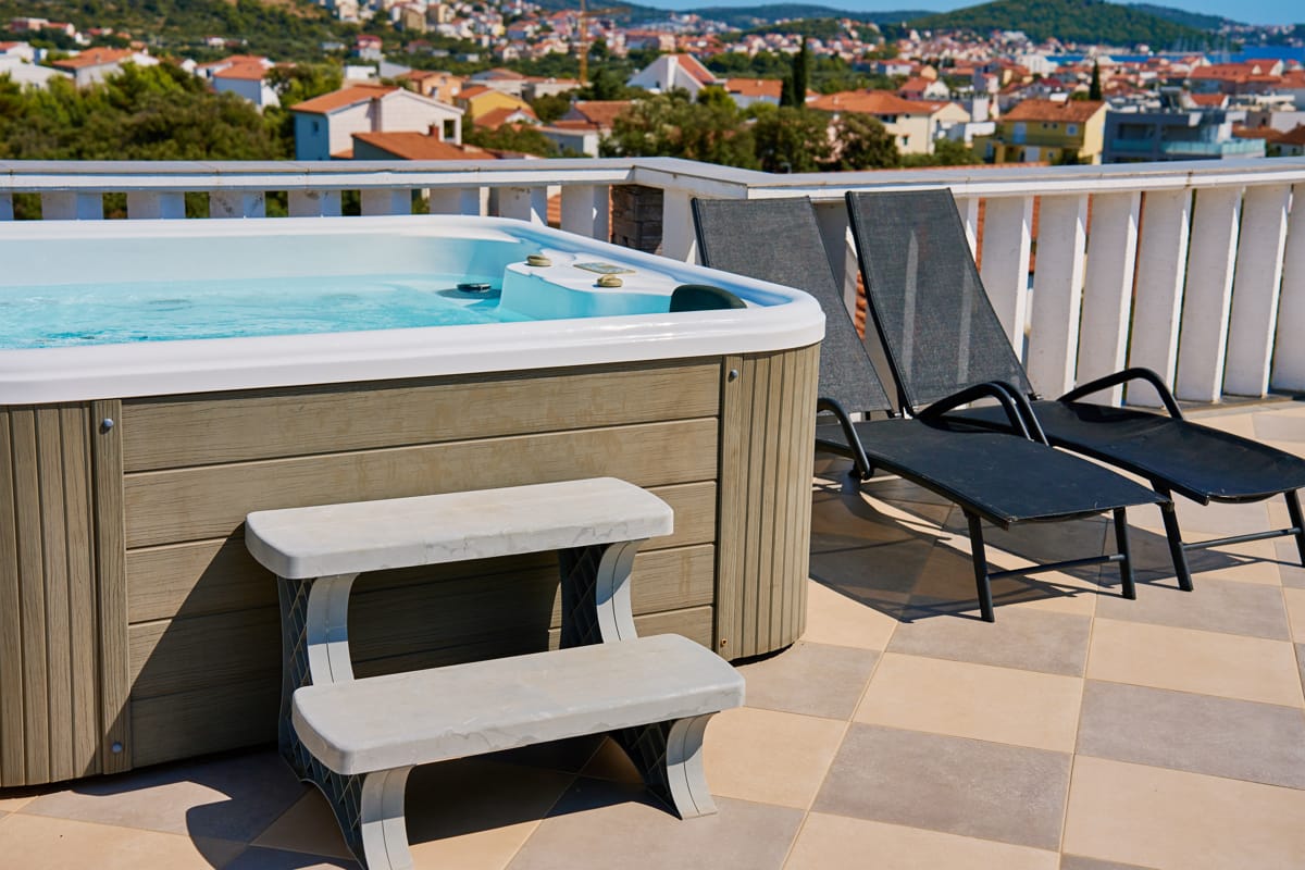 Jacuzzi exterior amplasat pe terasă, cu trepte de acces și șezlonguri, exemplu de spațiu corect ales pentru relaxare acasă