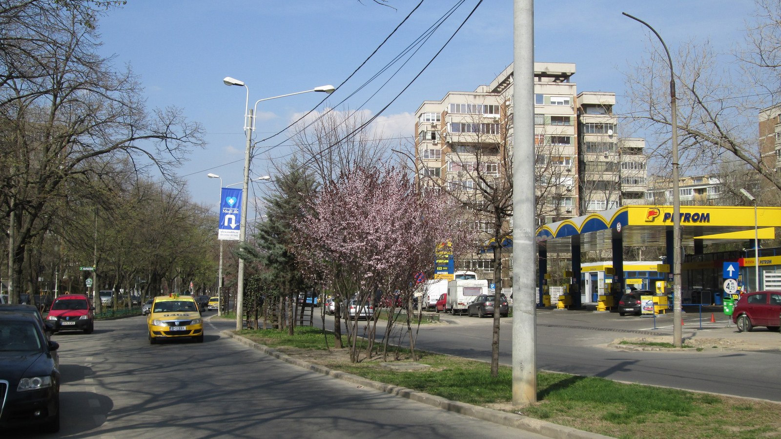 Stradă urbană cu blocuri de locuințe, trafic auto și spații verzi