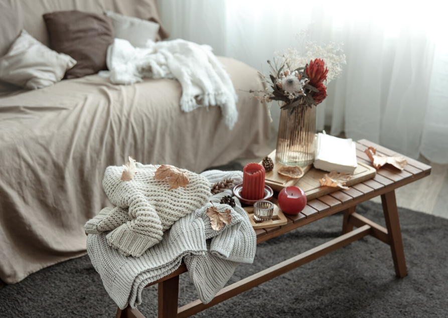 Living în tonuri neutre, cu perne decorative pe canapea, textile tricotate și decorațiuni de toamnă pe o măsuță din lemn.